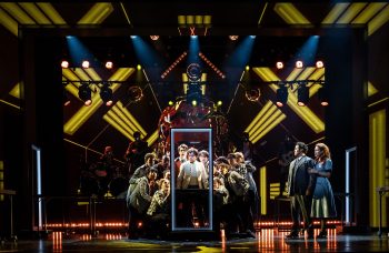A group of young men stare through an empty door frame in front of an elaborate stage set while a couple looks on nearby.