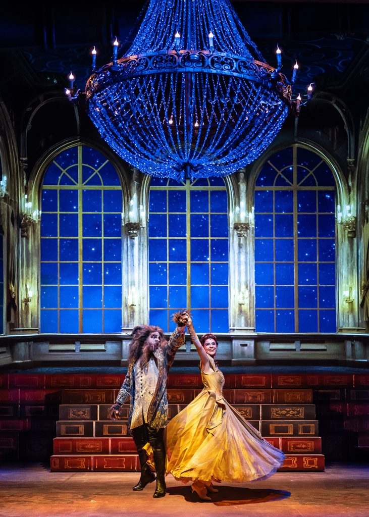 Belle and the Beast dance together under a chandelier.