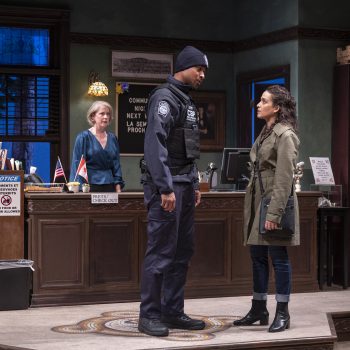 A woman and security guard look at each other in a library while a librarian looks at both from behind a check out desk.