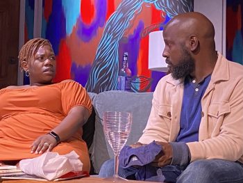A man and woman sit together on a couch in conversation.