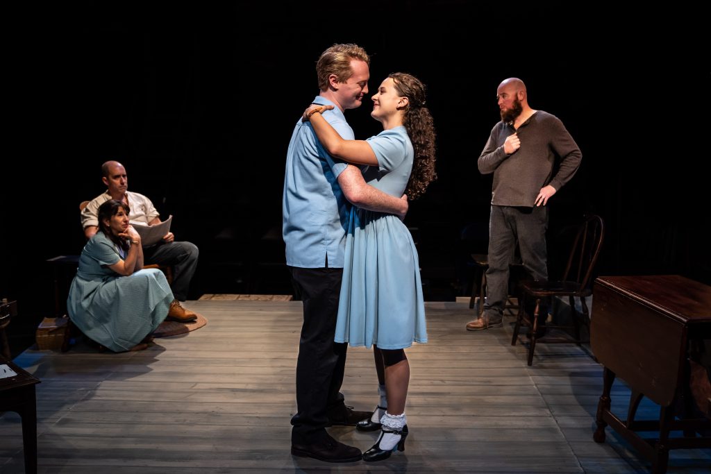A young man and woman dance center stage while family members watch from the back of the room.
