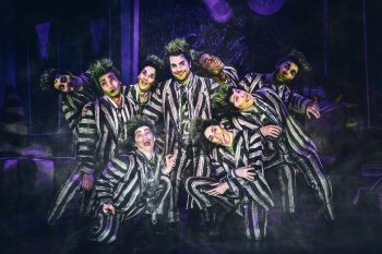 A group of actors dressed as Beetlejuice pose on stage.