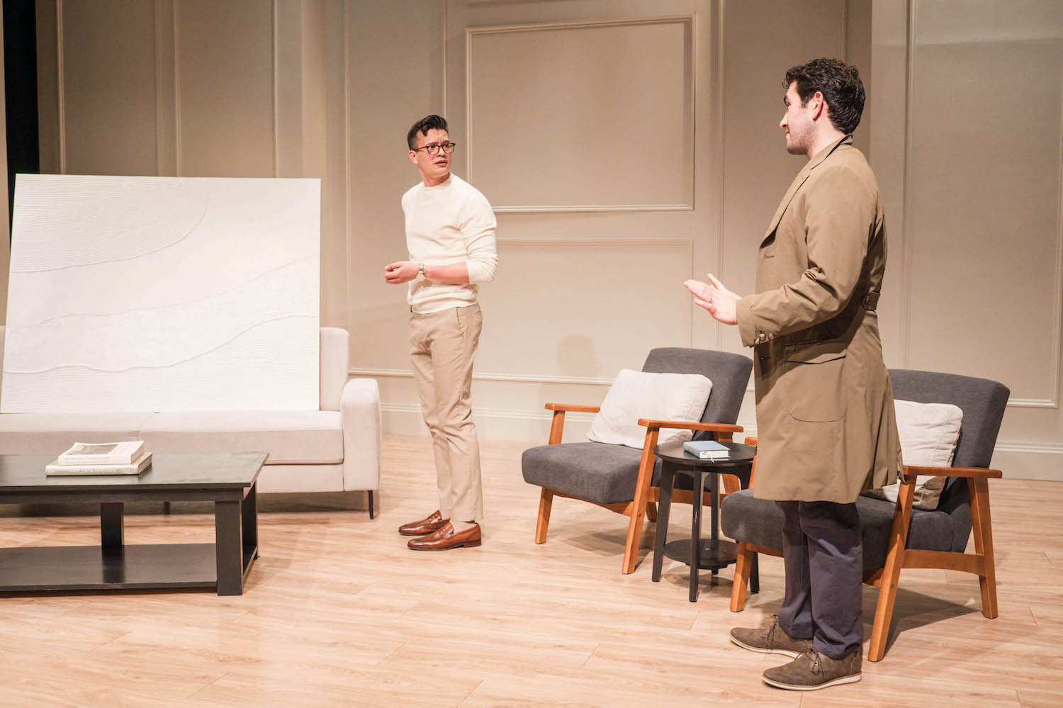 A man stands next to a white canvas while another man converses with him
